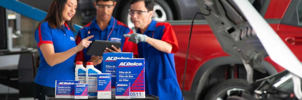 Três mecânicos conversando com os produtos da Acdelco na frente