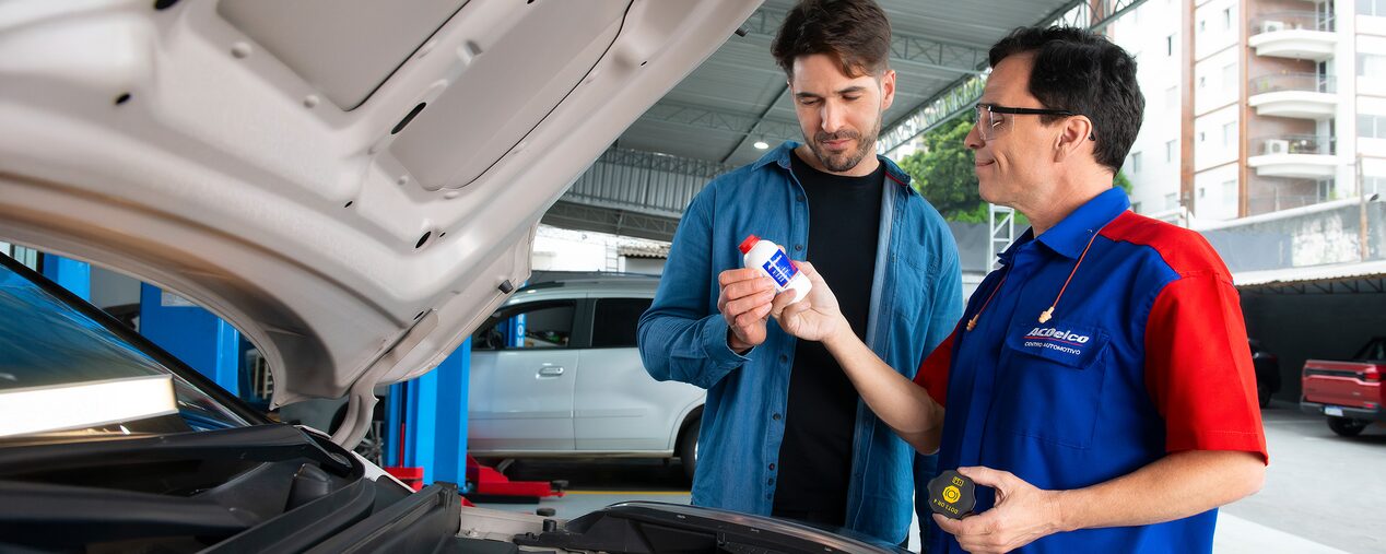 Mecánico mostrando envase de fluido ACDelco a cliente en taller.